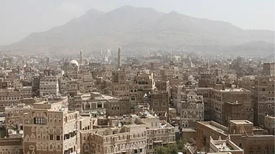 مدينة صنعاء (Sana'a City): مشهد بانورامي للمباني التاريخية في صنعاء القديمة مع جبال في الخلفية.