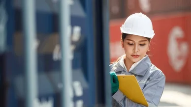 موظفة لوجستية تؤدي إحدى مهام المخلص الجمركي من خلال فحص المستندات بجانب حاوية شحن في الميناء.