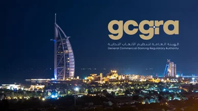 الهيئة العامة لتنظيم الألعاب التجارية في الإمارات مشهد ليلي لمدينة دبي يبرز فيه فندق برج العرب المضاء، وتظهر على الجانب الأيمن علامة الهيئة العامة لتنظيم الألعاب التجارية (gcgra) واسمها باللغتين العربية والإنجليزية باللونين الذهبي والأبيض.