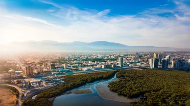 منظر جوي لمدينة ساحلية حديثة تتميز بوجود غابات المانغروف الخضراء وجبال في الأفق.