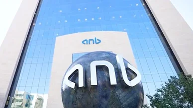 واجهة زجاجية شاهقة لمبنى البنك، يظهر عليها علامة (anb) باللون الأزرق، وأمامها مجسم كروي داكن كبير يحمل نفس العلامة بأحرف بيضاء ثلاثية الأبعاد.