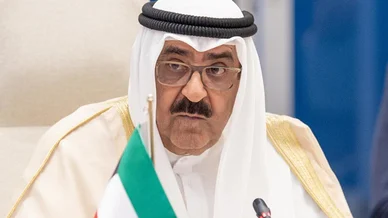 مسؤول خليجي أثناء مشاركته في اجتماع رسمي صورة لمسؤول خليجي رفيع المستوى يرتدي الزي التقليدي (الغترة البيضاء، العقال، والبشت) ونظارات طبية، يجلس في مؤتمر أو اجتماع رسمي مع وجود ميكروفون وجزء من علم دولة الكويت أمامه.