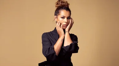 Portrait de Chimène Badi en robe noire, posant les mains sur son visage.