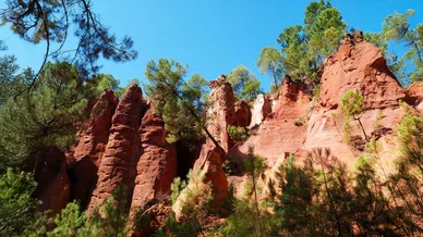 Rochers sculptés et formations naturelles du Sentier des Ocres à Roussillon. Falaises rouges du Sentier des Ocres entourées de pins sous un ciel clair.