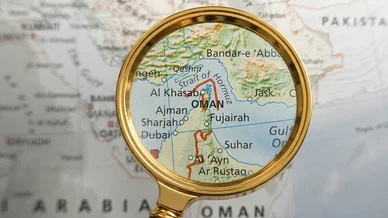 عدسة مكبرة تسلط الضوء على موقع مضيق هرمز الاستراتيجي على خريطة جغرافية.