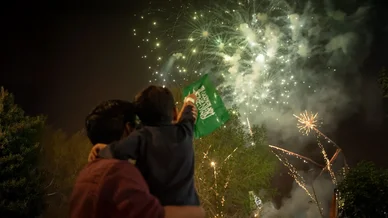 احتفالات الألعاب النارية وعلم السعودية الاحتفال برفع علم السعودية أمام عروض الألعاب النارية المضيئة في سماء الليل.