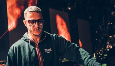 DJ Snake : Maître de la scène sous les feux de la rampe. DJ Snake performe sur scène avec des flammes et des lumières en arrière-plan.
