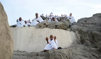 حجاج بملابس الإحرام يجلسون على الصخور المتعرجة وأحدهم يرفع يديه بخشوع للدعاء والتضرع.