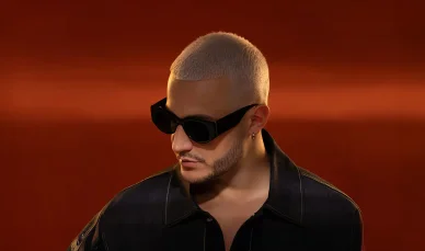 DJ Snake : Charisme éclatant sur fond rouge. DJ Snake avec des lunettes de soleil sur un fond rouge vibrant.