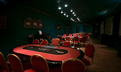 غرفة بوكر ذات إضاءة خافتة في كازينو، تتميز بطاولات لعب حمراء بيضاوية وكراسي مطابقة.
