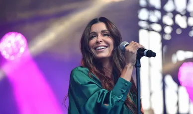 Un gros plan de la chanteuse Jenifer en concert. Jenifer radieuse chantant dans un micro sur une scène éclairée en rose.