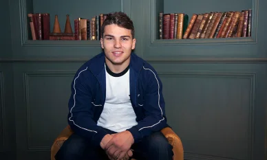 Antoine Dupont assis et souriant devant une bibliothèque.