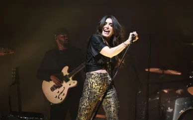 Une performance live captivante de la chanteuse Jenifer. Jenifer chantant avec énergie sur scène, vêtue d'un pantalon à motifs et d'un haut noir.