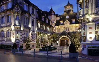 Façade illuminée de l'Hôtel Barrière Le Normandy à Deauville la nuit, une propriété emblématique du Groupe Barrière.