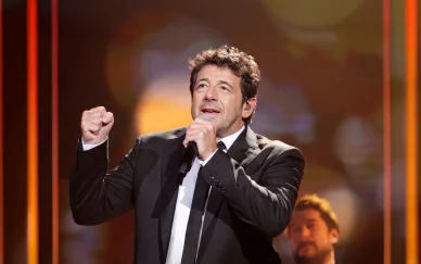 Patrick Bruel chantant sur scène en costume noir.