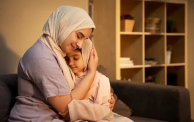 عناق أمومي دافئ بلمسة إسلامية لقطة قريبة لأم مسلمة تعانق ابنتها بحنان في المنزل. كلتاهما ترتديان الحجاب وعيناهما مغمضتان بسلام.