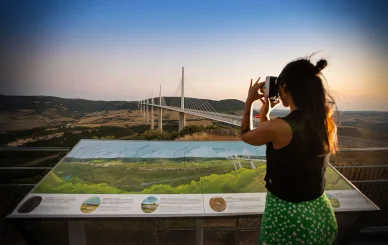 Femme photographiant le Viaduc de Millau depuis un point de vue panoramique.