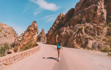 Route des Calanques de Piana, balade au cœur des falaises corses. Voyageuse sur la route sinueuse des Calanques de Piana, entre falaises rouges et ciel bleu.