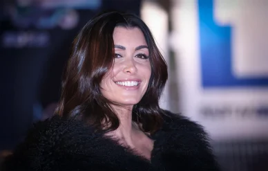 La chanteuse Jenifer arrivant à un événement public. Portrait de Jenifer avec un large sourire, portant un manteau de fourrure noire.