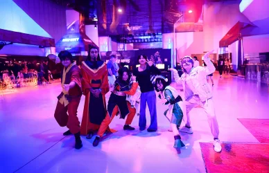 مجموعة شباب بأزياء كوسبلاي لشخصيات كرتونية يقفون لالتقاط صورة في معرض كوميك كون تحت إضاءة النيون.