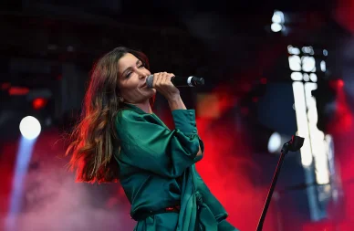 Jenifer chantant passionnément dans son micro lors d'un concert. La chanteuse Jenifer en pleine performance sur scène avec une chemise en soie verte.
