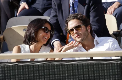 Florence Foresti souriante dans les tribunes, portant des lunettes de soleil, en compagnie de l'humoriste Alexandre Kominek.