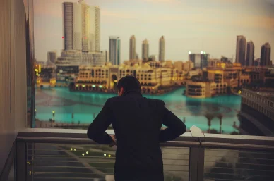 Pavel Dourov observant la ville depuis un balcon avec vue sur des gratte-ciel et un bassin turquoise.