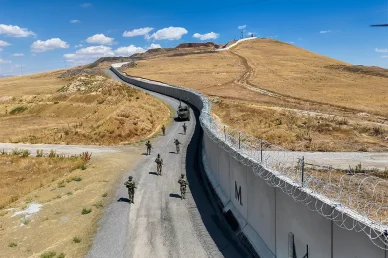 دوريات عسكرية وتعزيزات أمنية مشددة على طول الشريط الحدودي أمن الحدود (Border Security): دورية عسكرية مسلحة تحرس جداراً خرسانياً مزوداً بأسلاك شائكة.