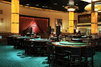 التصميم الداخلي لكازينو طنجة، يعرض طاولات لعب خضراء بكراسي سوداء، وأعمدة برتقالية مضيئة، ومسرحاً مزيناً بستائر حمراء تحمل شعار الكازينو في الخلفية.