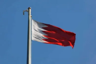 علم مملكة البحرين يرفرف عالياً علم البحرين الوطني باللونين الأحمر والأبيض يرفرف على سارية في سماء زرقاء صافية.