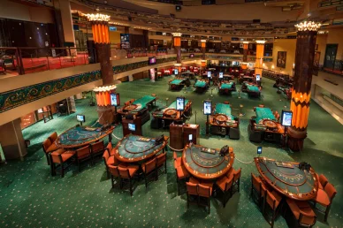 قاعة كازينو فخمة واسعة ذات عدة مستويات، تطل على العديد من طاولات القمار الخضراء والعديد من الشاشات الإلكترونية والكراسي البرتقالية، وتتميز بأعمدة مضيئة فخمة تشبه الشعلات.