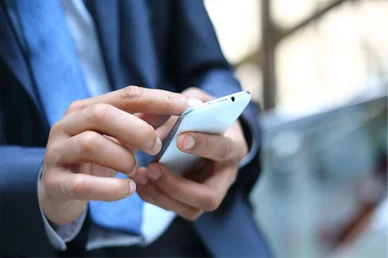 لقطة قريبة ليدي رجل أعمال يرتدي بدلة زرقاء ويستخدم هاتفاً ذكياً أبيض اللون لتصفح التطبيقات الرقمية.