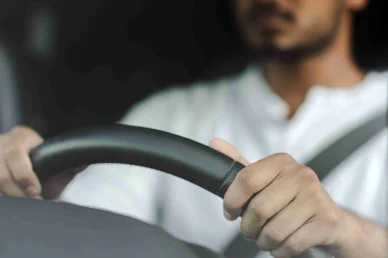دعاء للرحلات القصيرة قيادة آمنة: يدان تمسكان بعجلة قيادة سيارة لرجل يرتدي حزام الأمان