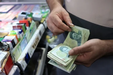 التعاملات التجارية اليومية وحركة النقد في متاجر التجزئة الريال الإيراني (Iranian Rial): بائع يحسب رزمة من الأوراق النقدية فوق عداد متجر لبيع التبغ.