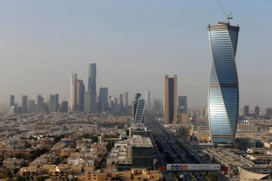 منظر جوي لمدينة الرياض يبرز برج المجدول الملتوي يميناً وناطحات سحاب مركز الملك عبدالله المالي في الخلفية مع طريق مزدحم.