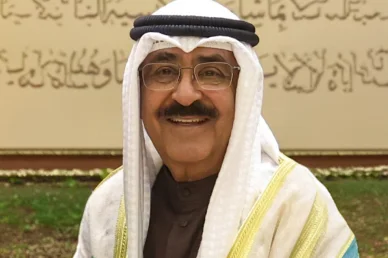 صورة شخصية لمسؤول خليجي مبتسم بزي تقليدي صورة مقربة لمسؤول خليجي رفيع المستوى يبتسم، يرتدي الزي التقليدي (الغترة البيضاء، العقال، والبشت) ونظارات طبية، مع خلفية تظهر فيها لوحة مزينة بخط عربي أنيق.