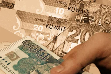 يد تمسك بورقة نقدية من فئة 1000 روبية باكستانية مع أوراق نقدية من فئتي 10 و20 دينار كويتي في الخلفية.