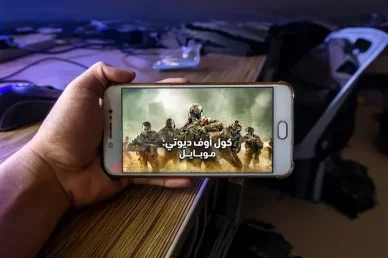 لعبة كول أوف ديوتي موبايل: تجربة ألعاب التصويب المثيرة على الهواتف الذكية يد تمسك بهاتف ذكي أبيض يعرض شاشة بداية لعبة كول أوف ديوتي موبايل التي تظهر مجموعة من الجنود