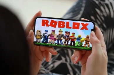 لعبة روبلوكس على الموبايل شخص يمسك هاتفاً ذكياً يعرض لعبة روبلوكس وشخصياتها
