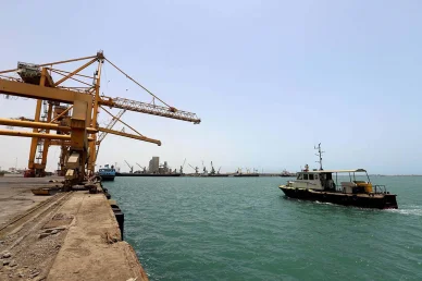 ميناء الحديدة: البنية التحتية للشحن والنشاط الملاحي في اليمن ميناء الحديدة (Hodeidah Port): رافعات جسرية صفراء وقارب بحري في ميناء الحديدة باليمن.