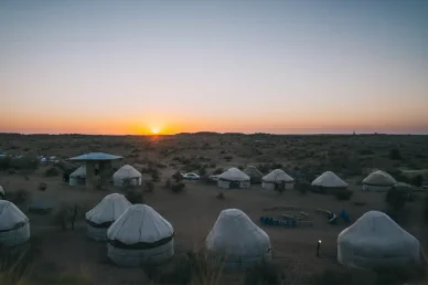مخيم صحراوي يضم خياماً تقليدية وسط طبيعة هادئة وقت غروب الشمس، وجهة مميزة للسياحة.