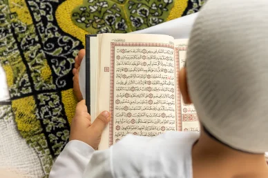 تلاوة القرآن الكريم: خشوع وطمأنينة في قراءة سورة المطففين شخص مسلم يرتدي زياً أبيض ويقرأ سورة المطففين من القرآن الكريم بتدبر أثناء جلوسه على سجادة الصلاة