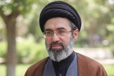 رجل الدين الإيراني مجتبى خامنئي صورة شخصية لرجل الدين الإيراني مجتبى خامنئي يرتدي عمامة سوداء ونظارات طبية وعباءة بنية وخلفه أشجار خضراء.