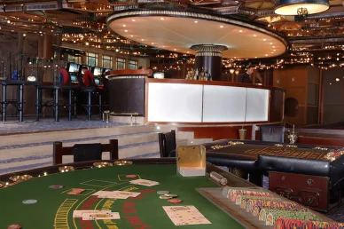 كازينو سميراميس: استمتع بألعاب الطاولة الكلاسيكية في أجواء راقية كازينو سميراميس (Casino Semiramis): طاولة بلاك جاك وفيشات اللعب مع بار الكازينو في الخلفية.
