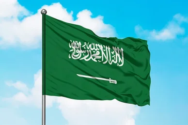 علم المملكة العربية السعودية الأخضر يرفرف على سارية تحت سماء زرقاء تتخللها بعض السحب.
