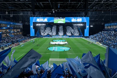دعم جماهيري استثنائي: تيفو "WIN" يزين مدرجات الهلال مشهد مهيب لجماهير نادي الهلال في المدرجات يشكلون تيفو بكلمة "WIN" باللونين الأبيض والأزرق مع شاشات عملاقة تعرض اسم النادي وأعلام ترفرف في المقدمة