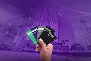 يد تحمل مجموعة من بطاقات الدفع الرقمي (stc pay) بألوان متنوعة، مثل الأخضر والبنفسجي والأسود، أمام خلفية بنفسجية تدمج معالم معمارية شهيرة من دول الخليج العربي.