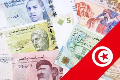 العملة الوطنية وعلم الجمهورية التونسية مجموعة متنوعة من الأوراق النقدية التونسية من فئات مختلفة، مع جزء من علم تونس الأحمر بنجمته وهلاله يغطي الجانب الأيمن من الصورة.