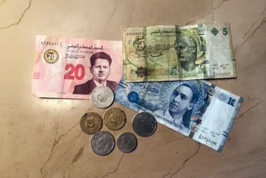 فئات مختلفة من العملة التونسية أوراق نقدية تونسية من فئات 5 و 10 و 20 ديناراً موضوعة بجانب مجموعة من العملات المعدنية المتنوعة على سطح رخامي.