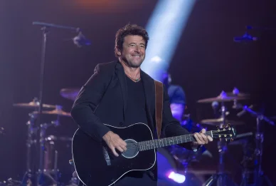 Patrick Bruel souriant avec une guitare sur scène.